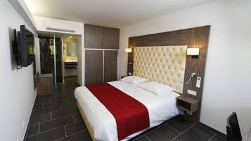 Quarto de hotel moderno com uma cama grande, televisão, banheiro e uma mesinha de cabeceira com abajur.