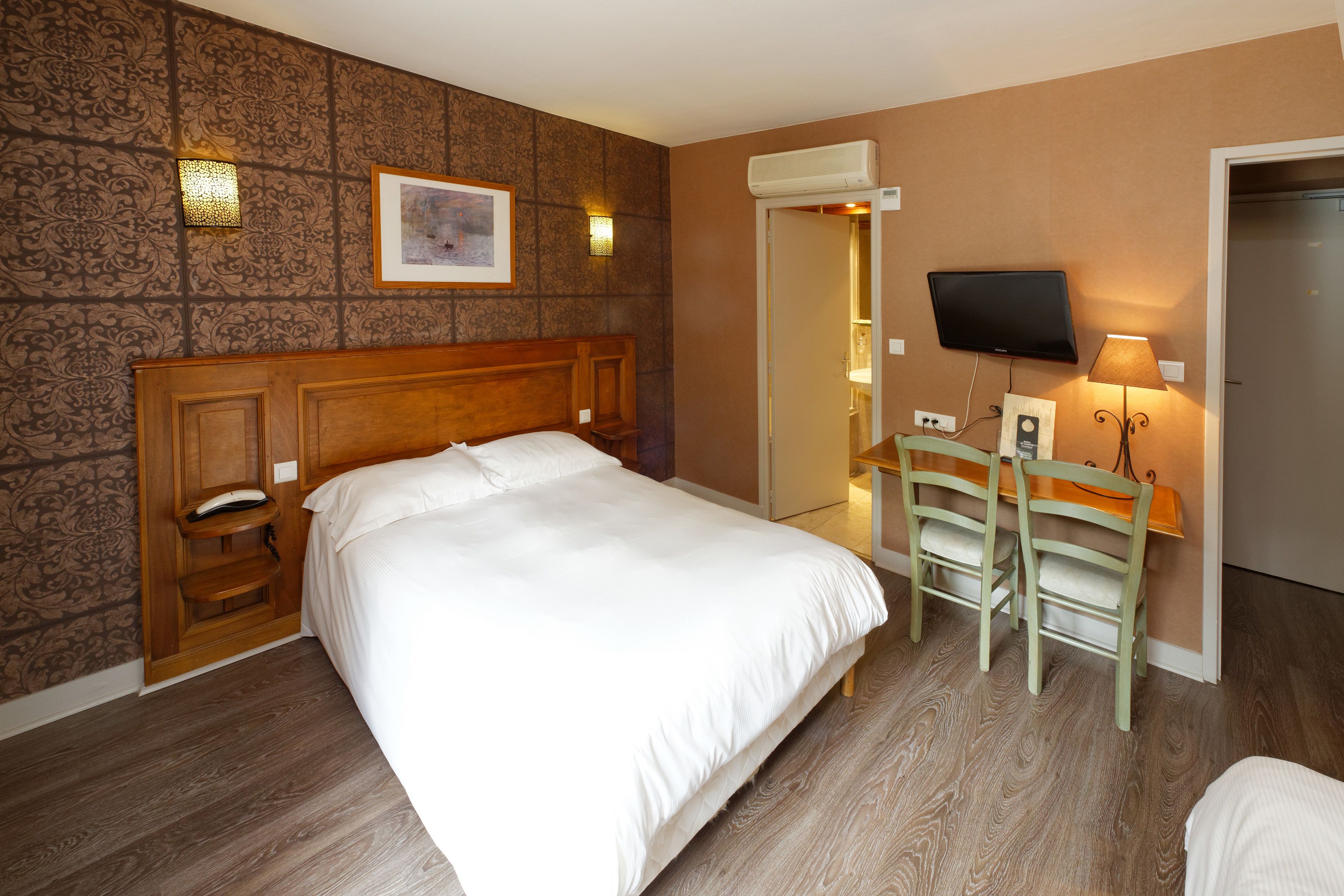 Habitación de hotel con una cama grande, cabecera de madera, escritorio con dos sillas, televisor de pantalla plana y aire acondicionado instalado en la pared.