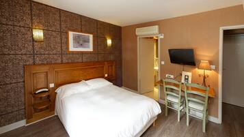 Habitación de hotel con una cama grande, cabecera de madera, escritorio con dos sillas, televisor de pantalla plana y aire acondicionado instalado en la pared.
