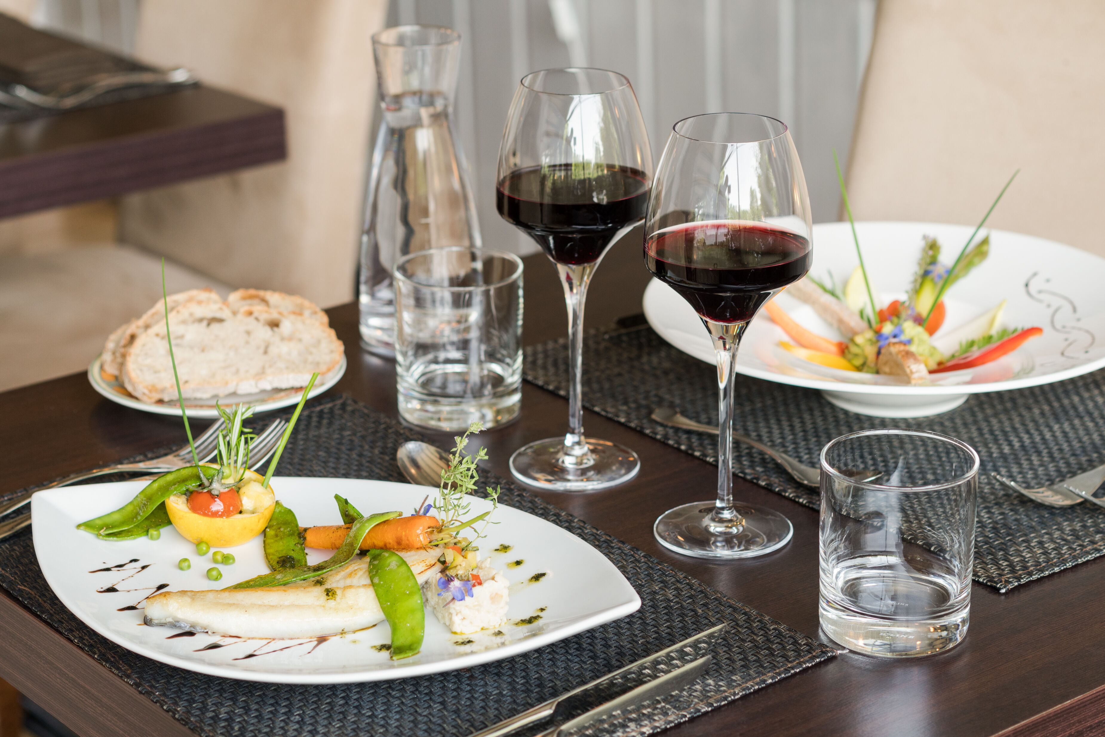 A dining table with plates of food, wine glasses, and cutlery.