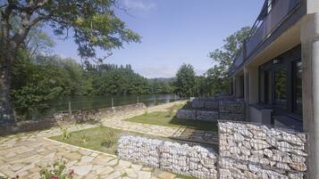 Un patio de piedra con vistas a un río, paredes de piedra y un edificio con grandes ventanales.