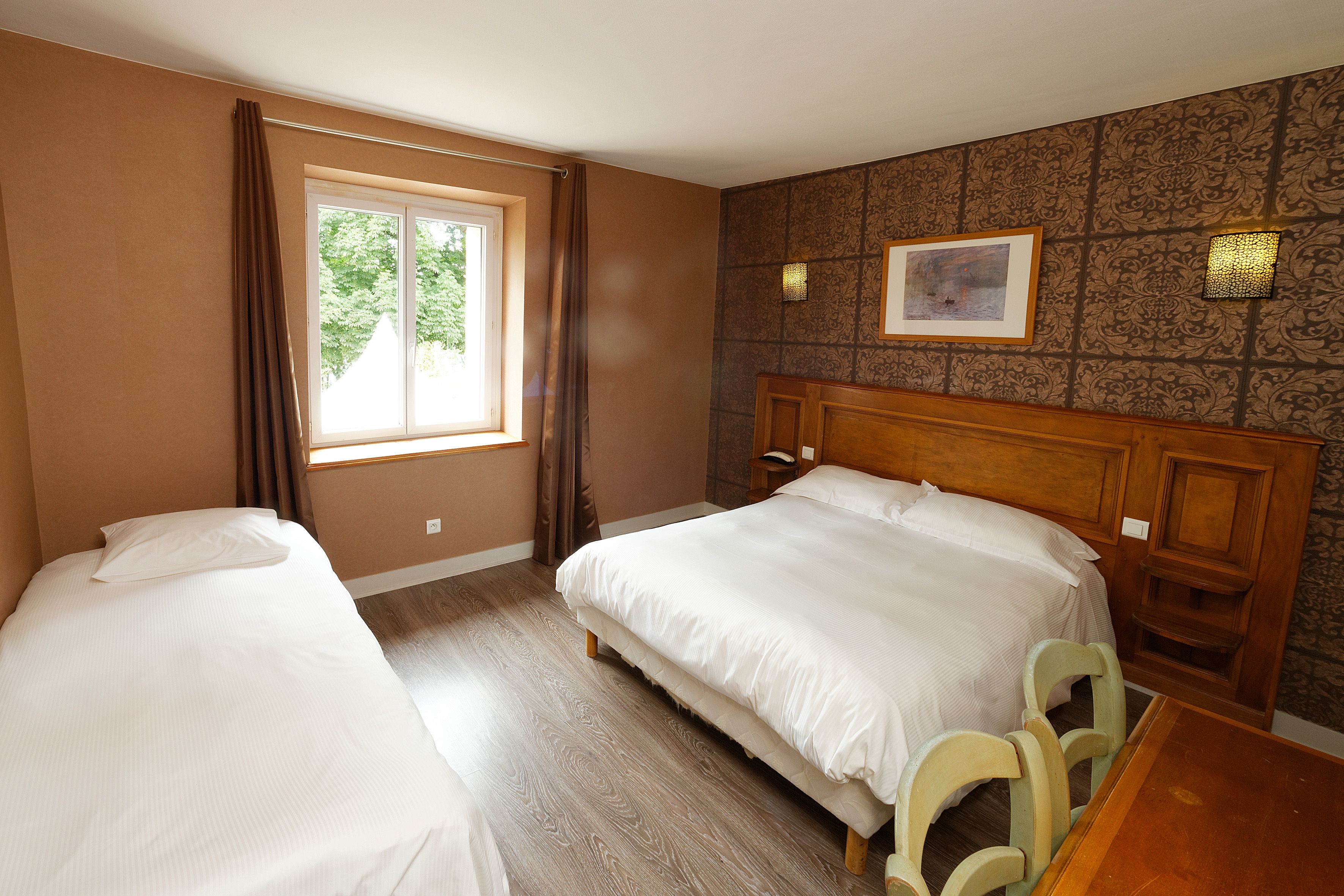 Een hotelkamer met twee enkele bedden, een raam met gordijnen, een kamer met een patroon op de muur en een houten hoofdeinde.
