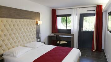 Une chambre d’hôtel avec une tête de lit capitonnée, un bureau avec une chaise, un lit avec une literie blanche et rouge, et une fenêtre avec des rideaux rouges.