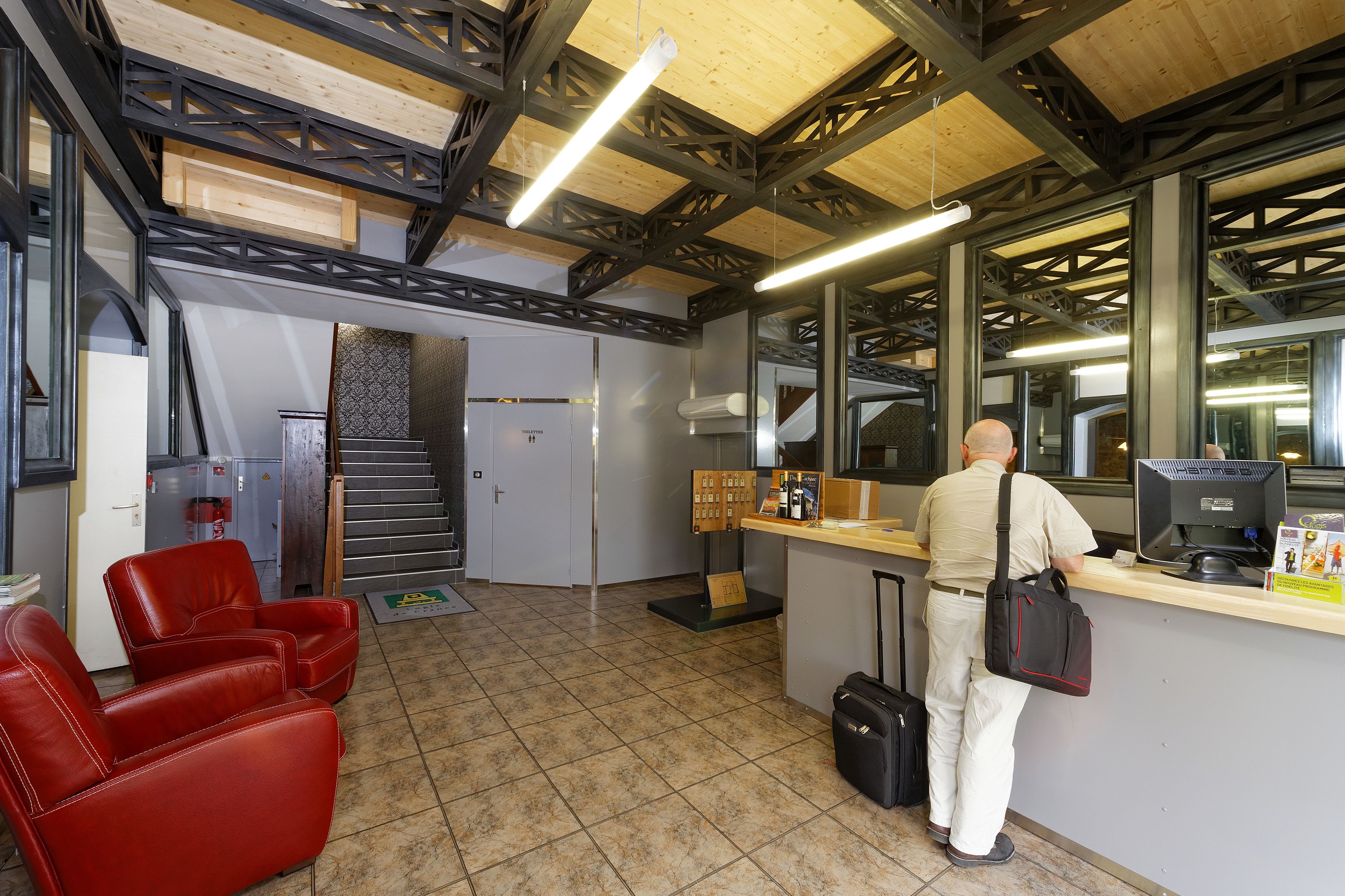 A reception area with a counter, a man standing at the counter, and red chairs in the foreground.