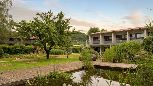 A serene garden with a pond, wooden deck, and a building with a balcony. - Hotel du Lac Foix (Foix)