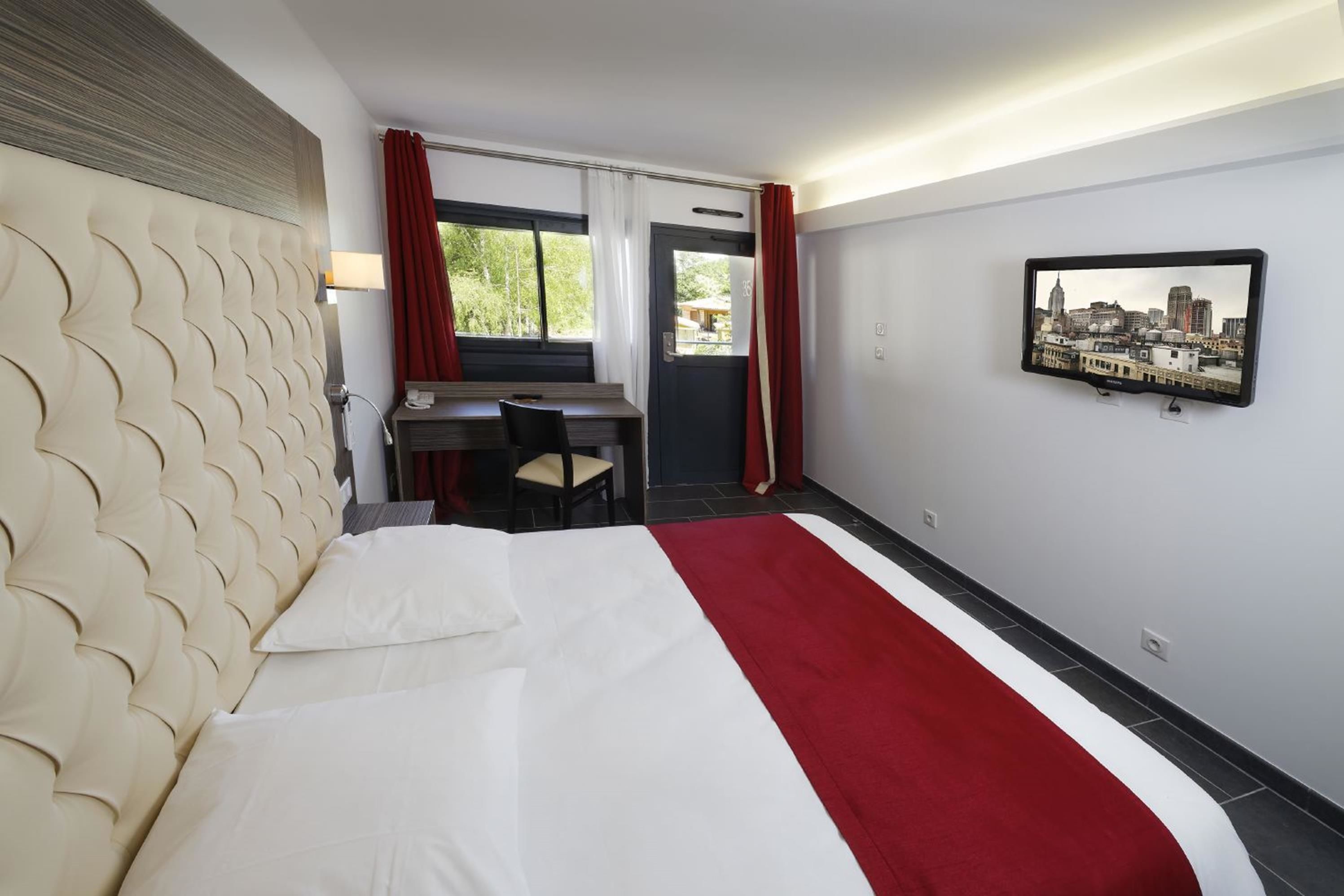 A hotel room with a large bed, a desk, and a cityscape view.