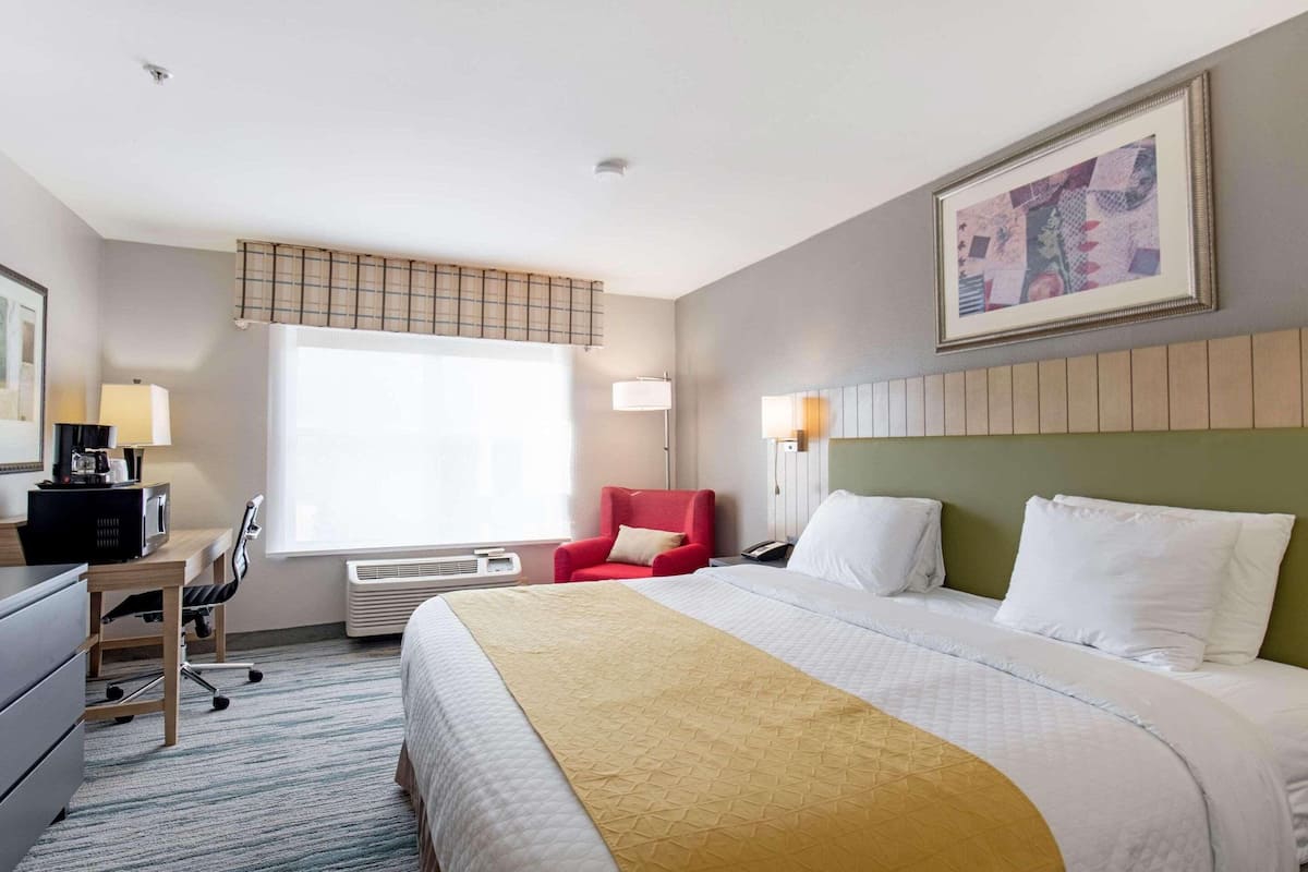 A hotel room with a bed, a desk, a chair, a window, and a painting on the wall.