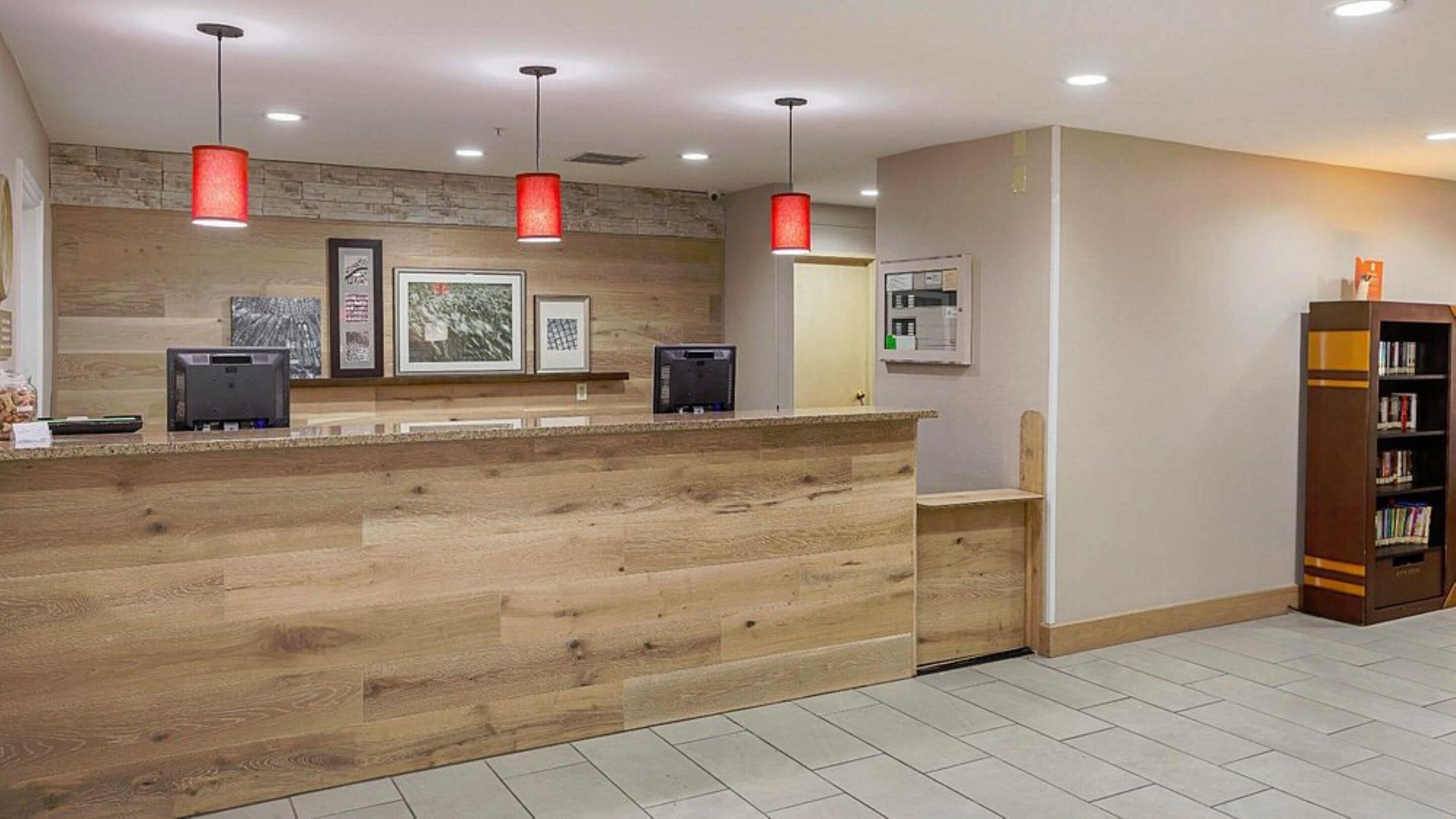 A reception desk with a wooden finish, overhead red pendant lighting, framed artwork on the wall, and a bookshelf to the right.