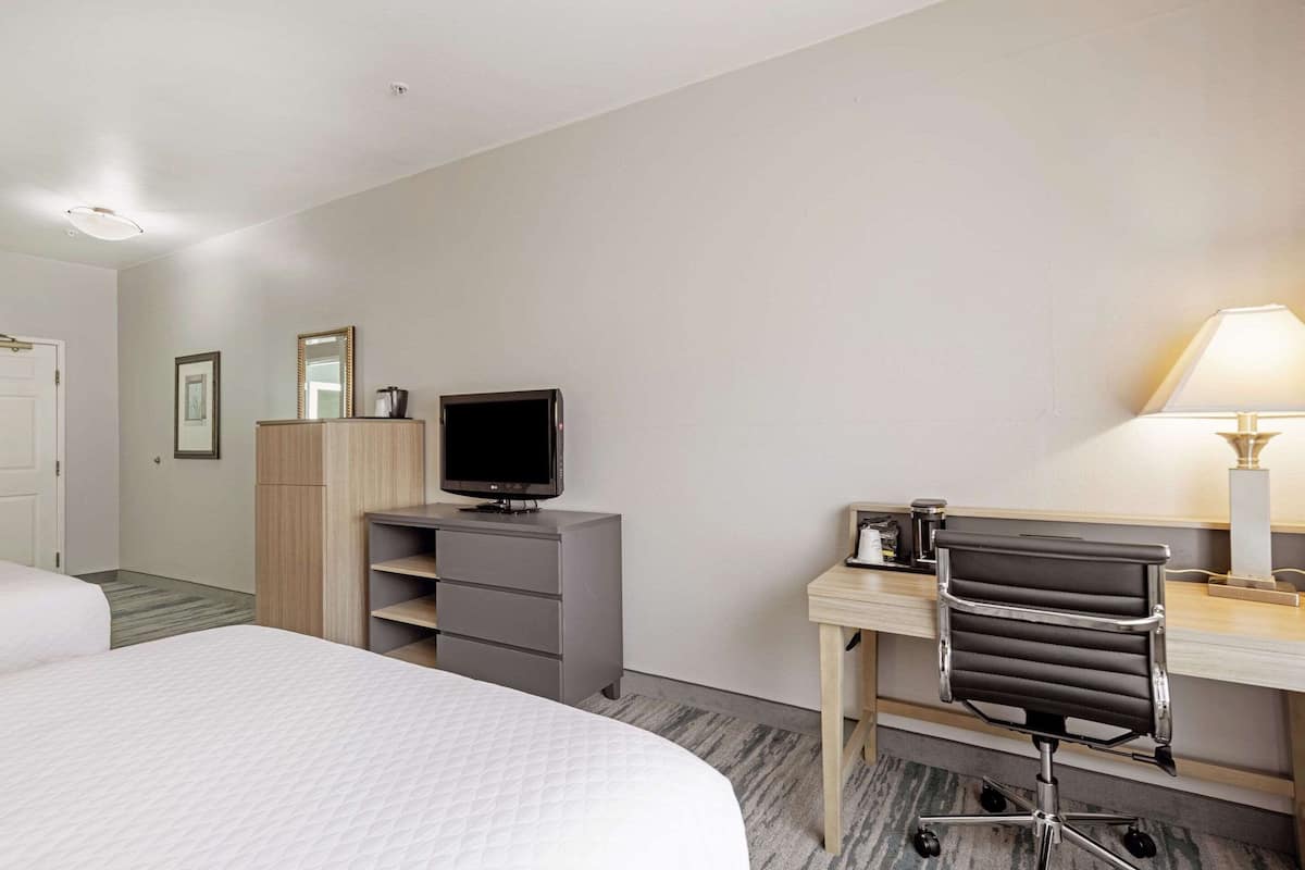 A hotel room with a bed, a desk with a chair, a television, and a lamp.