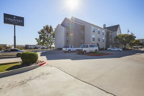 A Country Inn & Suites by Carlson with a parking lot, a signboard, and a building with multiple windows and a flag.