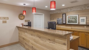A reception desk with a wooden counter, a clock, and framed artwork on the wall. - SureStay by Best Western Lewisville Dallas (Lewisville)