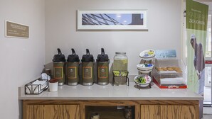 A breakfast bar with coffee makers, a fruit bowl, and a sign for PGA TOUR PRO Zach Johnson. - SureStay by Best Western Lewisville Dallas (Lewisville)