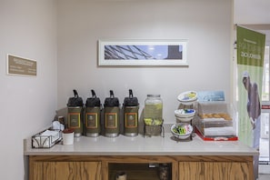 A breakfast bar with coffee makers, a fruit bowl, and a sign for PGA TOUR PRO Zach Johnson. - SureStay by Best Western Lewisville Dallas (Lewisville)