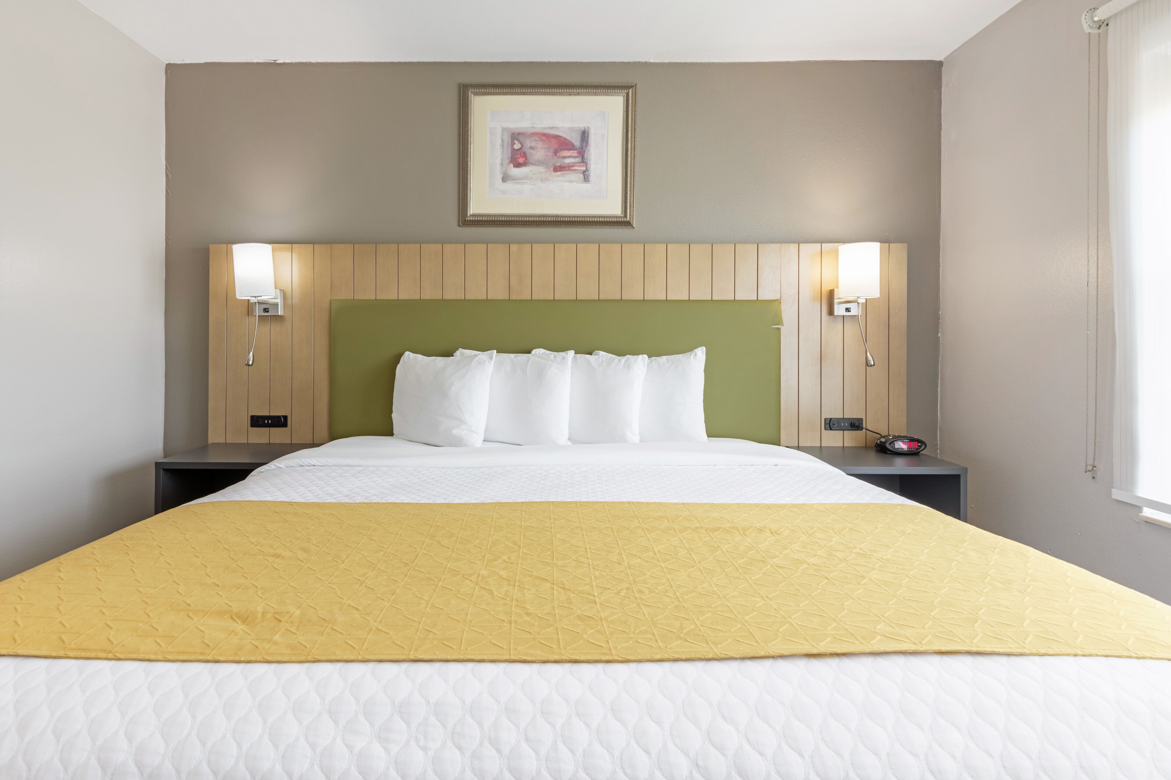 Hotelkamer met een groot bed, een groen hoofdeinde, twee bedlampen en een ingelijst schilderij boven het bed.