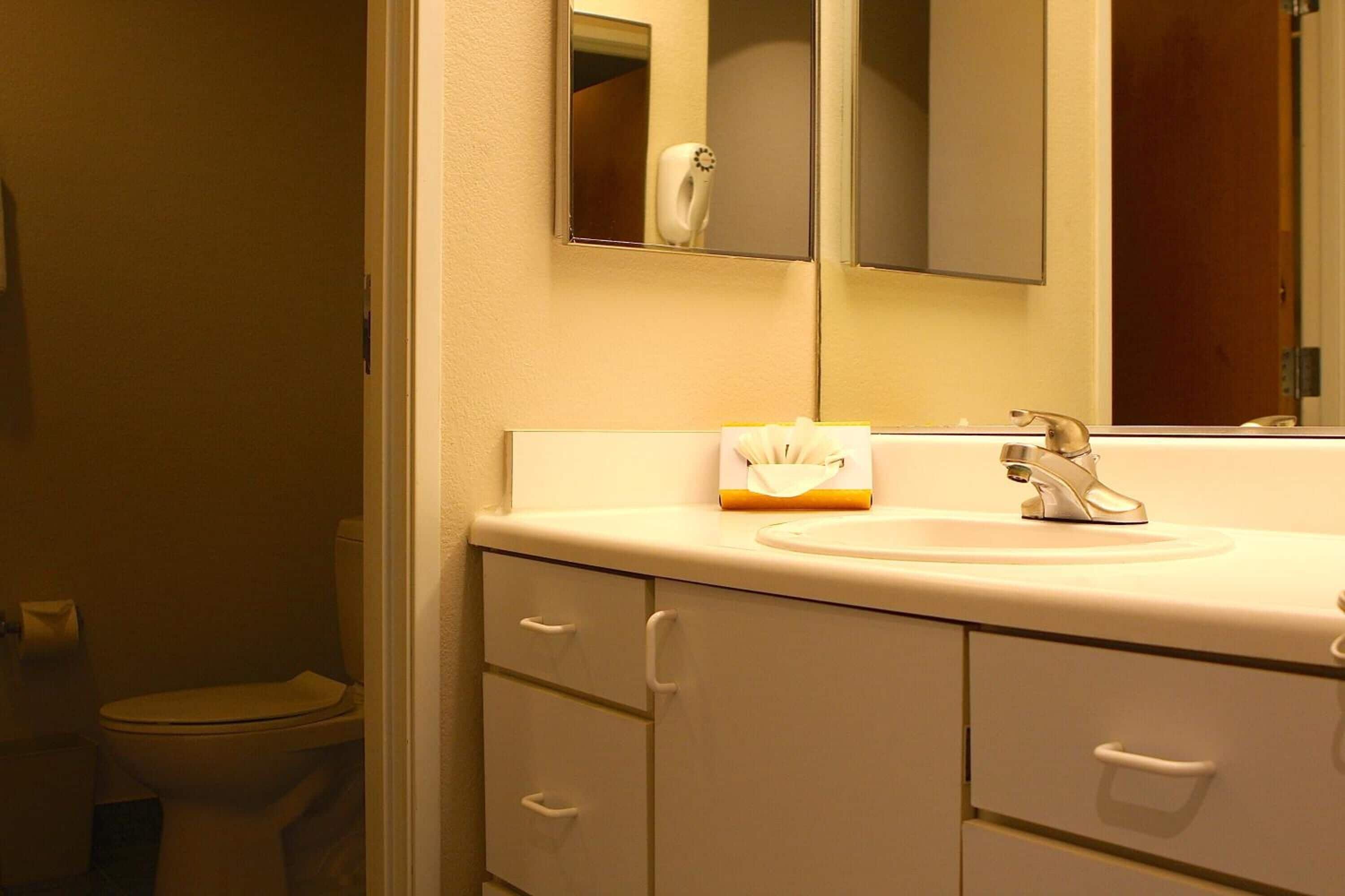 A bathroom with a toilet, a sink, a mirror, and a cabinet with drawers.