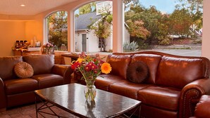 Amplia sala de estar con un sofá de cuero, una mesa de centro de vidrio y vistas a un jardín a través de amplias ventanas.