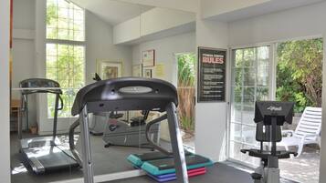 A gym with treadmills, a stationary bike, and a rowing machine. There are large windows and a door leading outside.