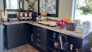 Una cocina con encimera de mármol, armarios oscuros, una estación de café y un frutero.