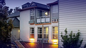 Una casa de dos pisos con un balcón, una escalera y dos ventanas iluminadas.