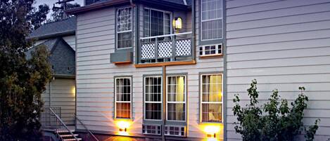 A two-story house with a balcony, a staircase, and two lit windows.