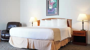 A hotel room with a large bed, two bedside tables with lamps, a leather armchair, and a framed artwork on the wall.