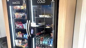 Un distributeur automatique divisé en deux sections, étiquetées « EN-CAS » et « BOISSONS FRAÎCHES », contenant divers en-cas et boissons.
