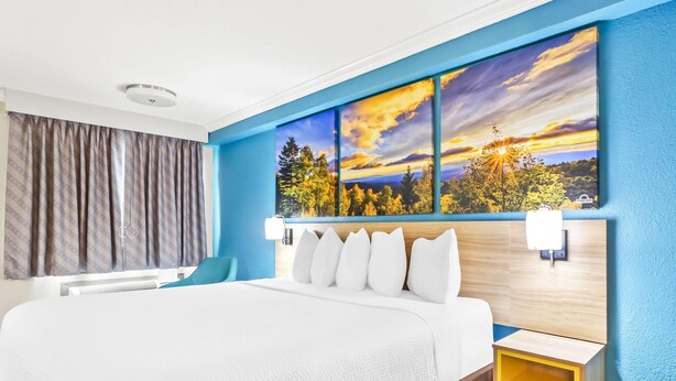 Une chambre d’hôtel avec un grand lit, une table de chevet, un bureau et une vue sur le coucher de soleil par la fenêtre.