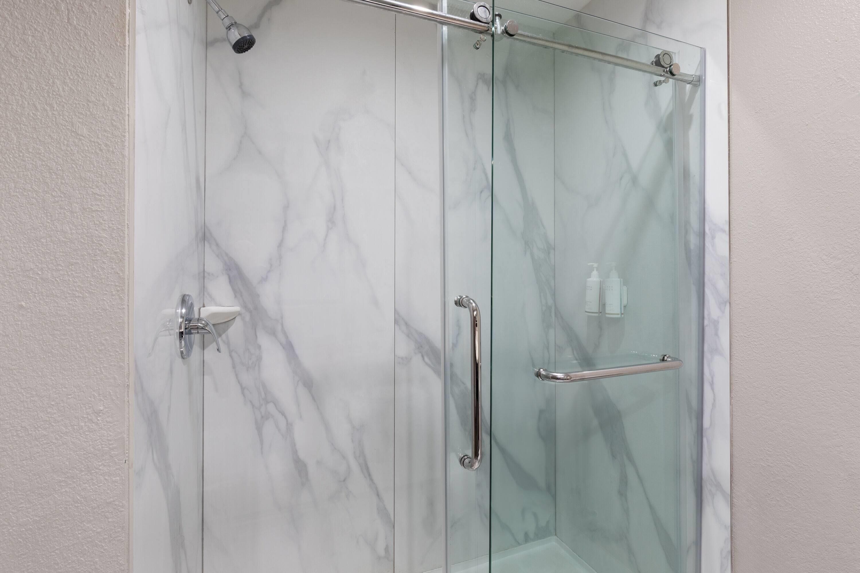 A glass-enclosed shower with marble walls and a handrail.