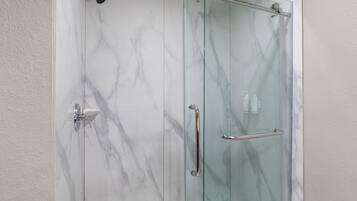 A glass-enclosed shower with marble walls and a handrail.