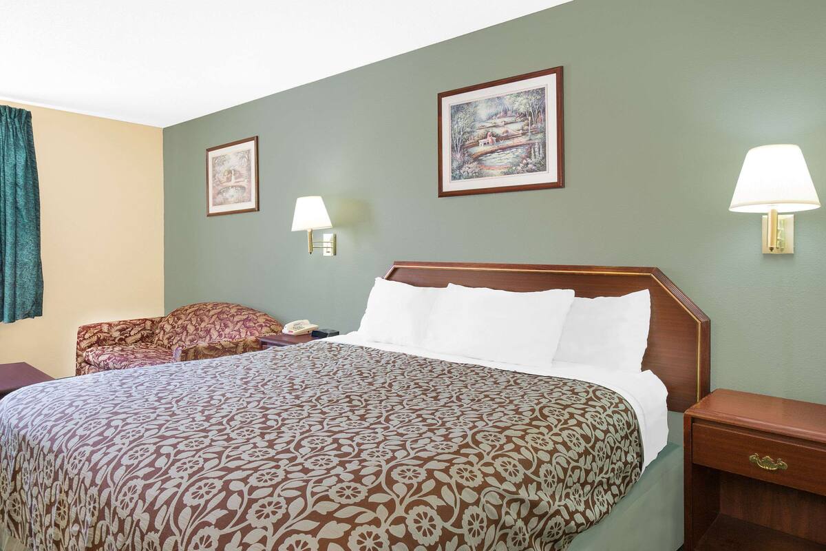 A hotel room with a large bed, two bedside lamps, a nightstand, a chair, and two framed pictures on the wall.