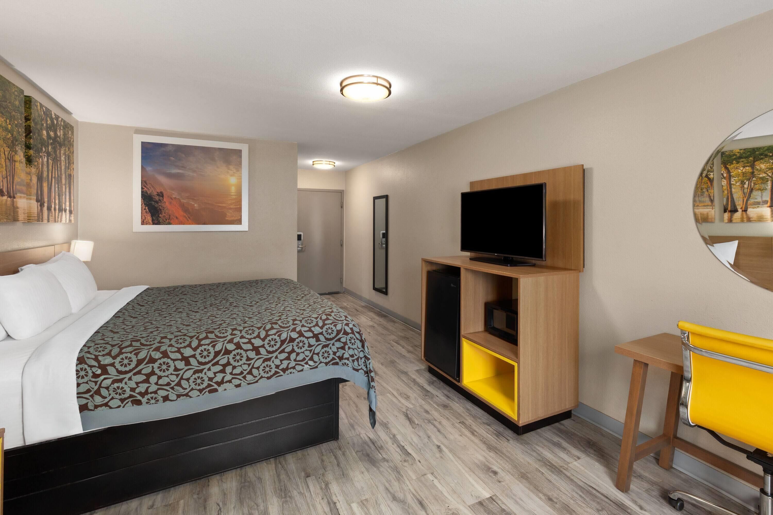 A hotel room with a bed, a TV on a wooden stand, a small table, and a mirror.