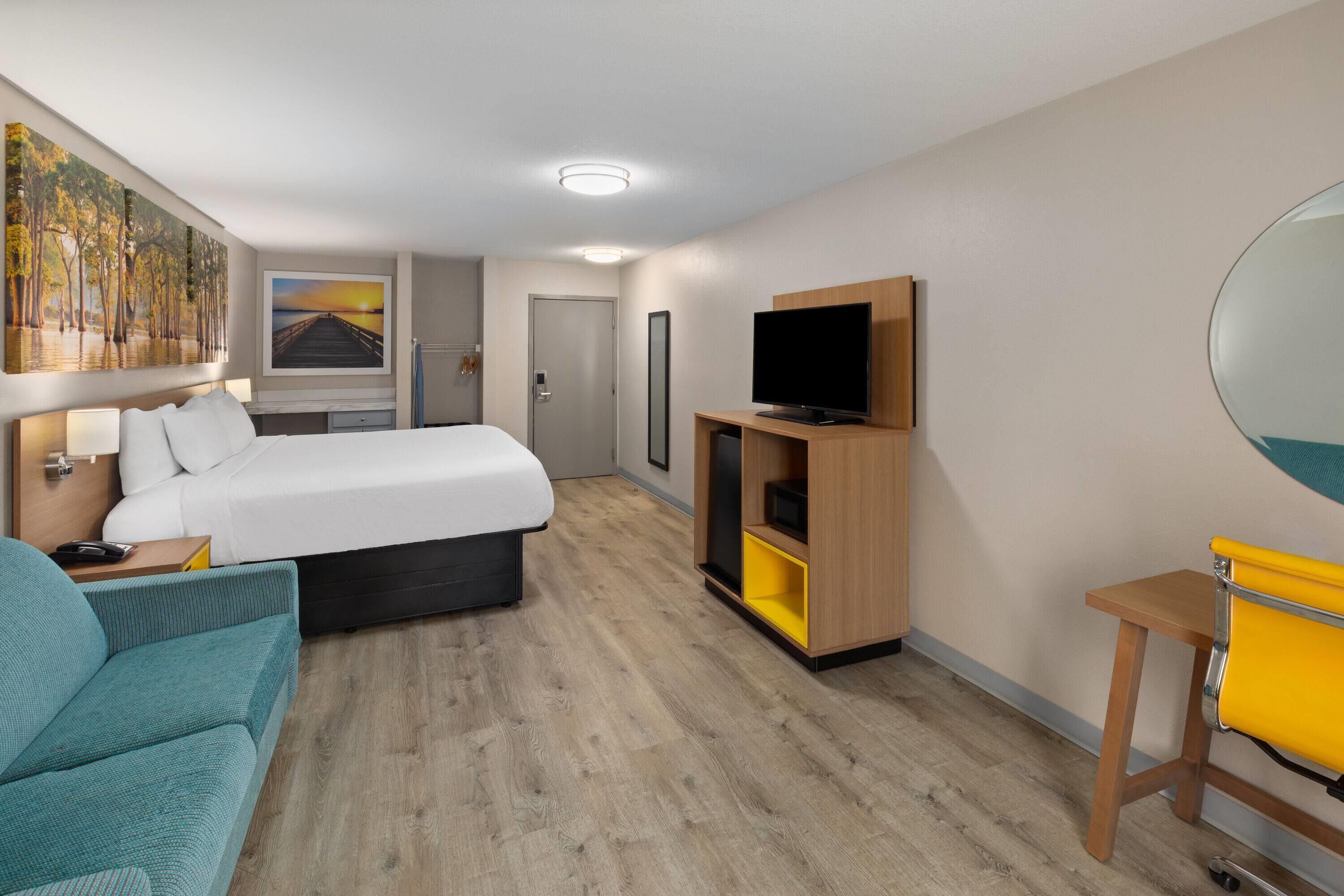 Une chambre d’hôtel avec un lit, une télévision, un bureau, une chaise et un tableau au mur.