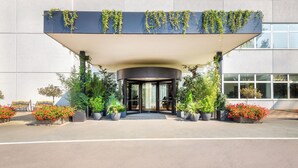Entrada moderna de un edificio con porche cubierto, plantas en macetas y vista despejada del interior.