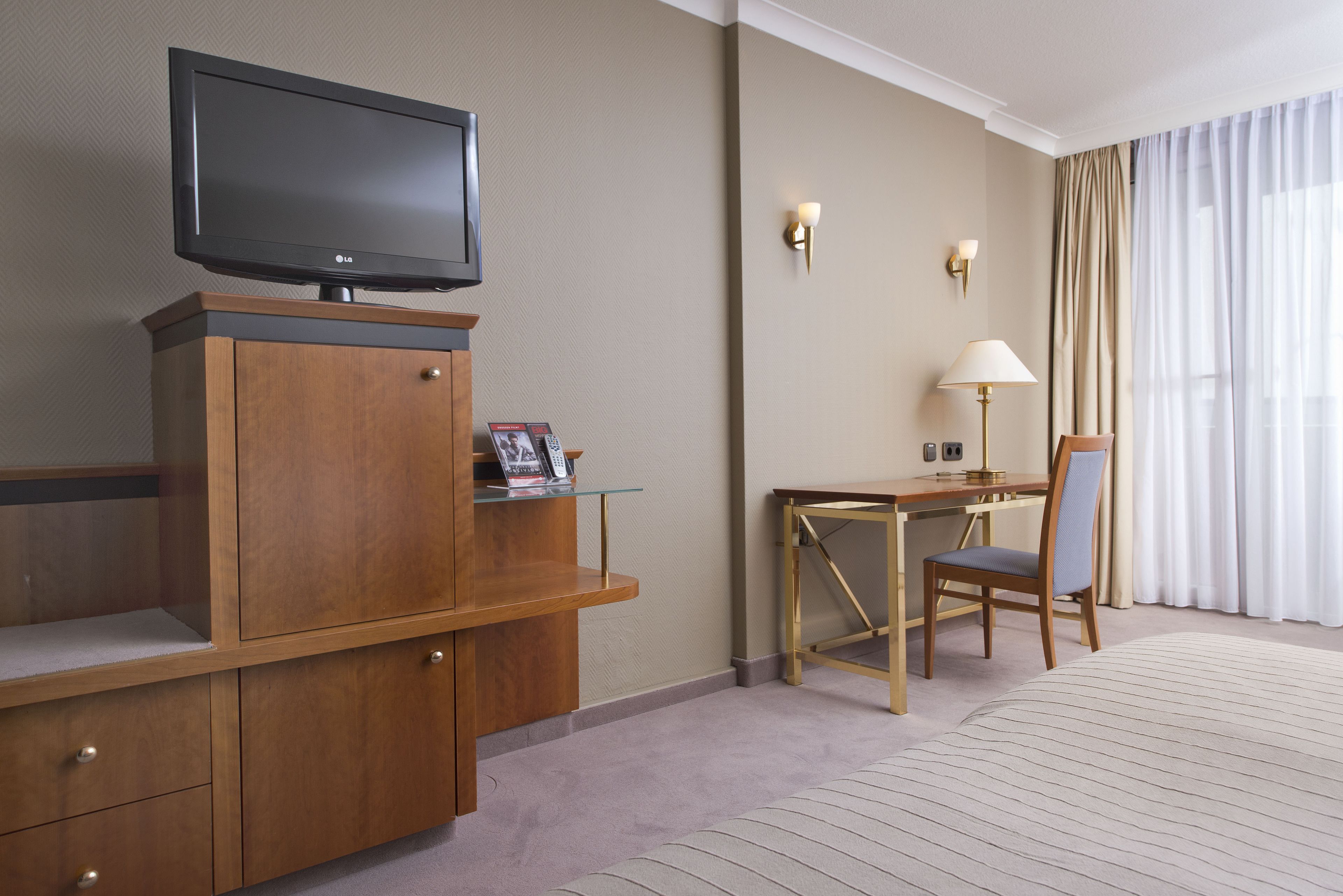 Une chambre d’hôtel équipée d’un téléviseur à écran plat posé sur un meuble en bois, d’un bureau avec une chaise, d’une lampe et d’un lit recouvert d’une courtepointe à rayures.