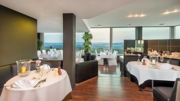 Un restaurante con mesas redondas, manteles blancos y vistas a la montaña.