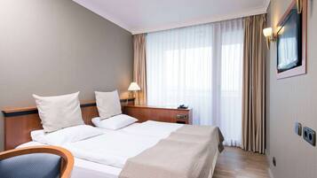 A hotel room with a large bed, a bedside table with a lamp, a chair, and a window with curtains.