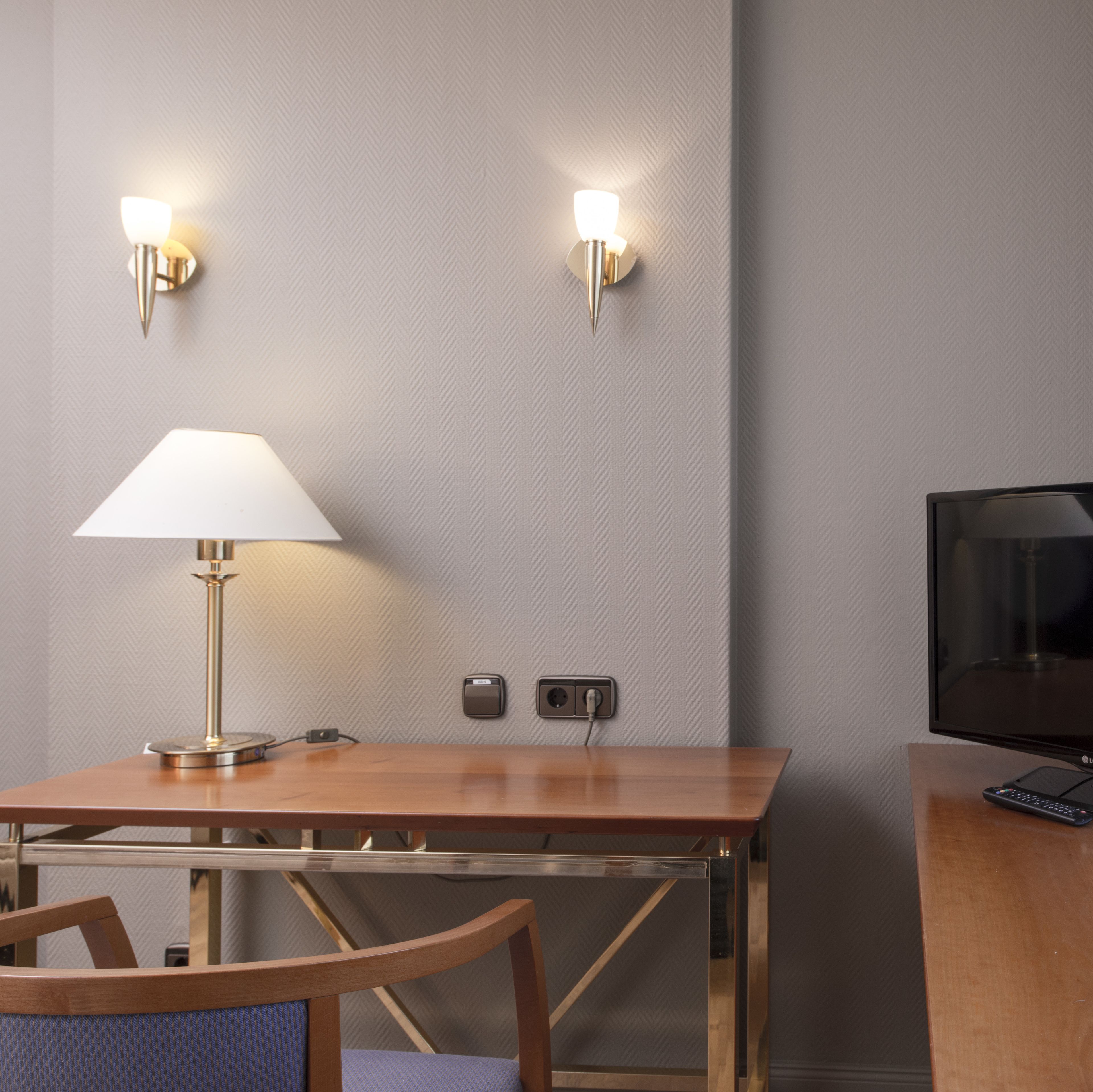 Habitación de hotel con un escritorio de madera, una lámpara, un televisor y dos luces empotradas.