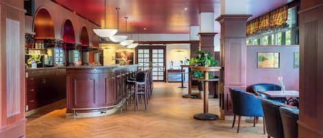 Un restaurante con zona de bar, suelo de madera y disposición de mesas y sillas.