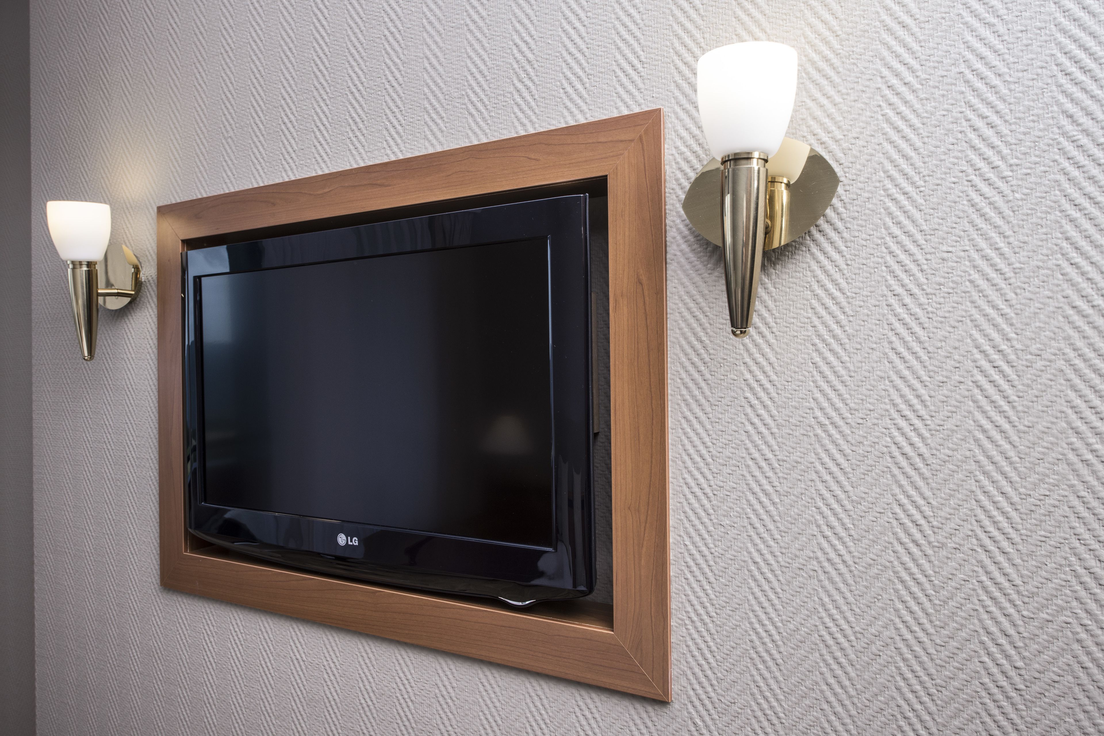 A flat-screen TV mounted on a textured wall with a wooden frame and two wall-mounted sconces.