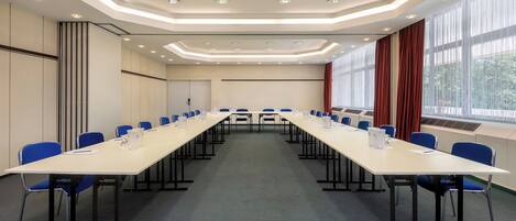 Una sala de conferencias con una larga mesa, sillas azules y piso alfombrado.