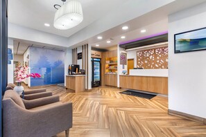 A modern reception area with a wooden herringbone floor, a reception desk, a seating area with chairs, and a decorative wall with a floral arrangement. - Sleep Inn (Manassas)