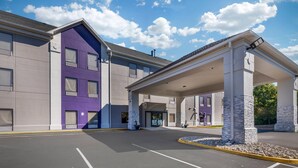 Un hôtel moderne doté d’une entrée couverte, d’un parking et offrant une vue sur un ciel bleu azur parsemé de nuages.