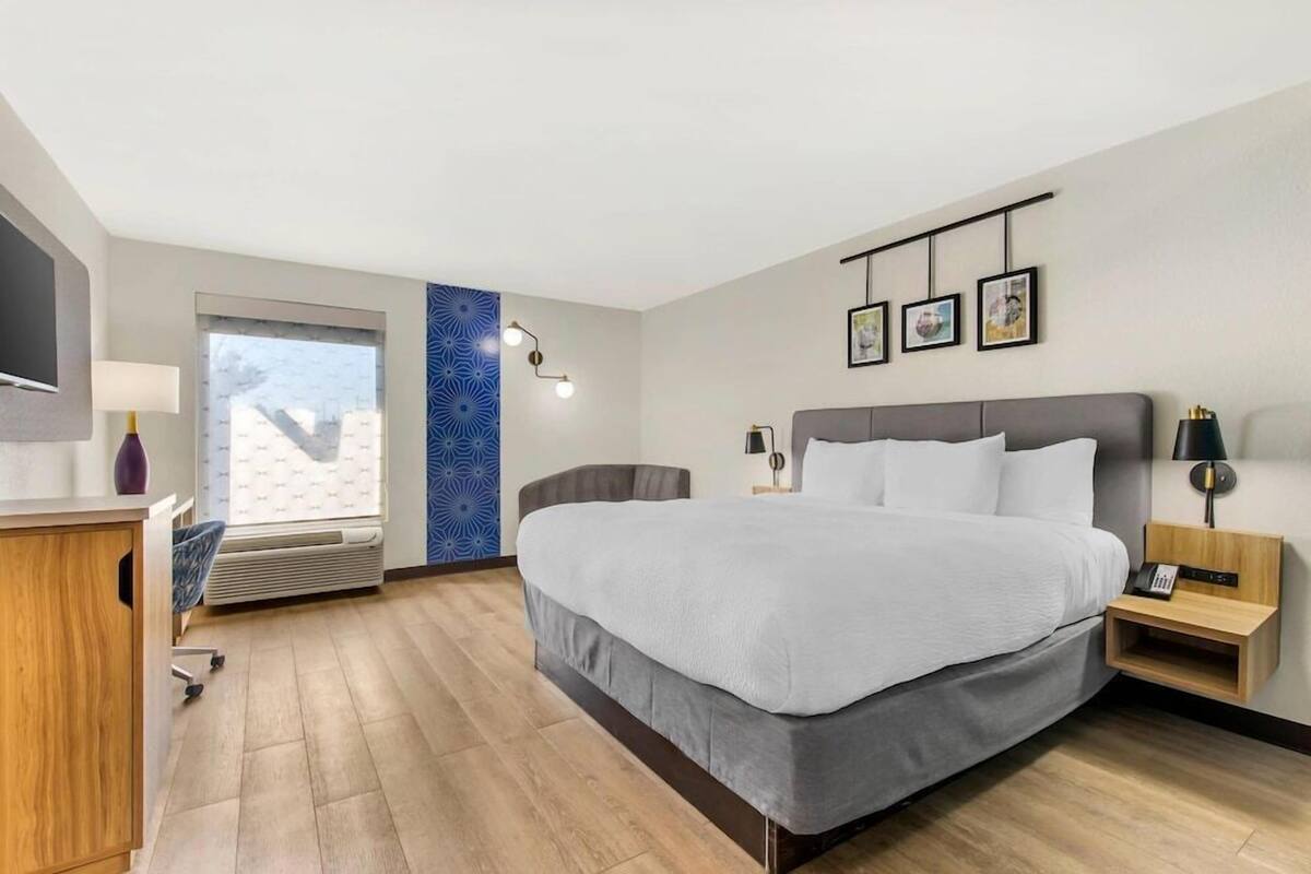 Une chambre d’hôtel avec un lit, des tables de chevet, une télévision, un bureau et une fenêtre.
