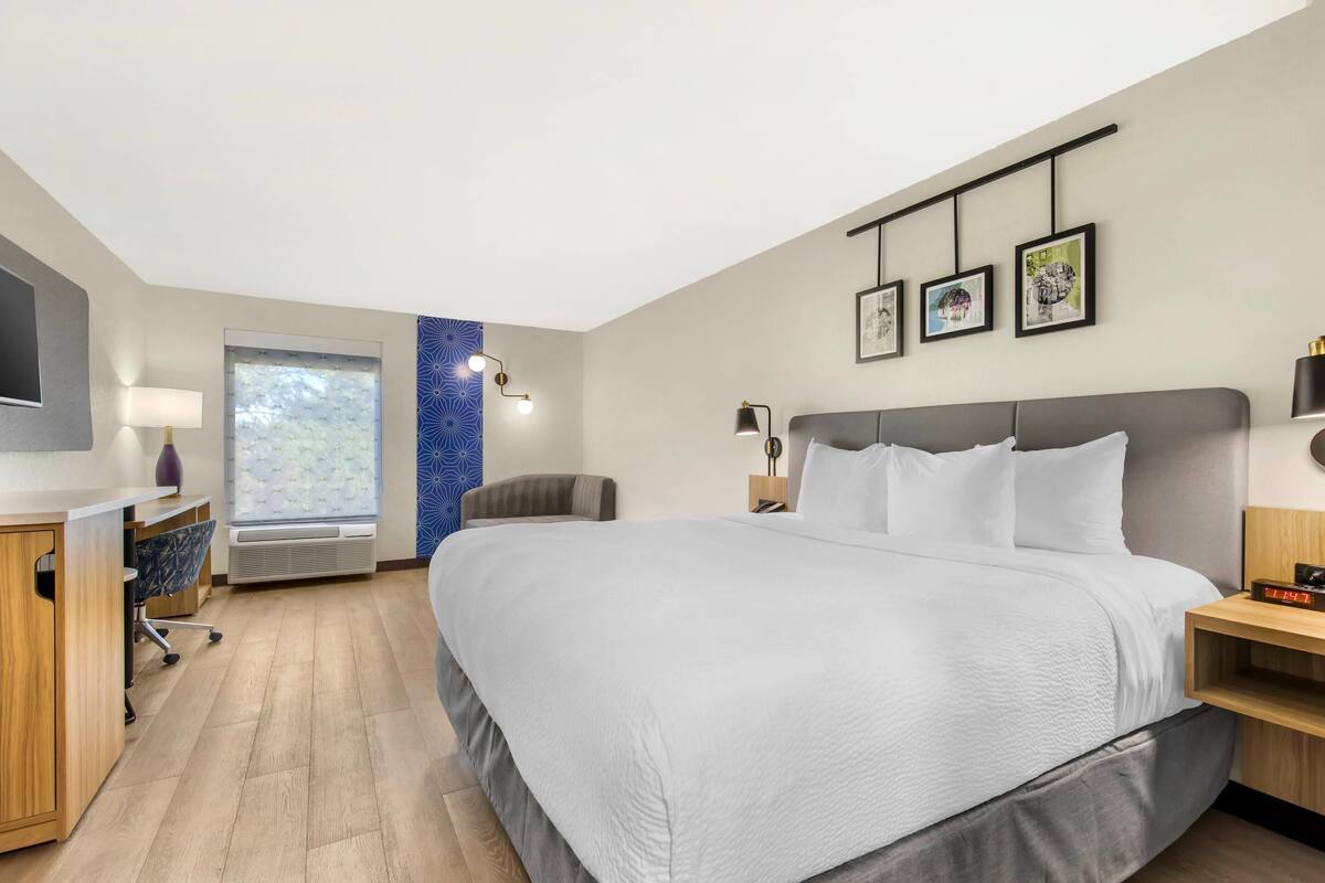 Une chambre d’hôtel moderne dotée d’un grand lit, d’un bureau, d’une chaise, d’une fenêtre offrant une vue agréable et d’œuvres d’art accrochées au mur.