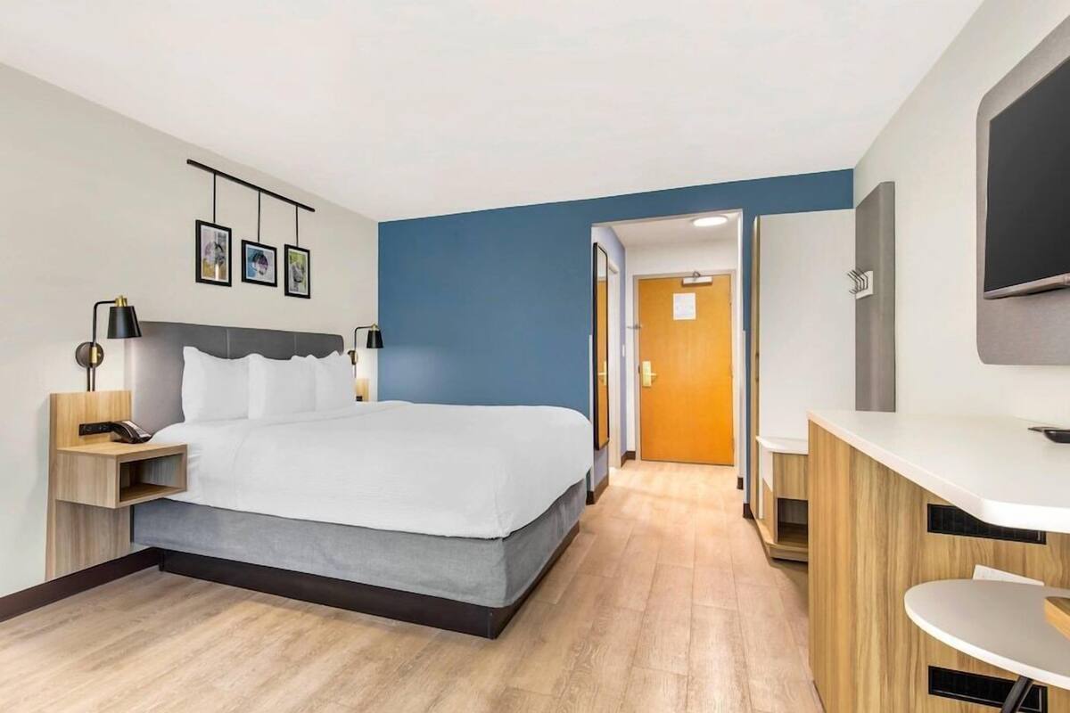 Une chambre d’hôtel moderne équipée d’un lit, d’une table de chevet, d’une lampe et d’un bureau avec une chaise.