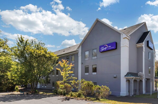 A Sleep Inn by Choice Hotels building with a modern design, featuring a prominent sign, a parking lot, and surrounding greenery. - Sleep Inn (Manassas)