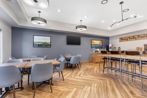 A modern conference room with wooden flooring, grey chairs, and tables. There are ceiling lights and a flat-screen TV mounted on the wall. - Sleep Inn (Manassas)