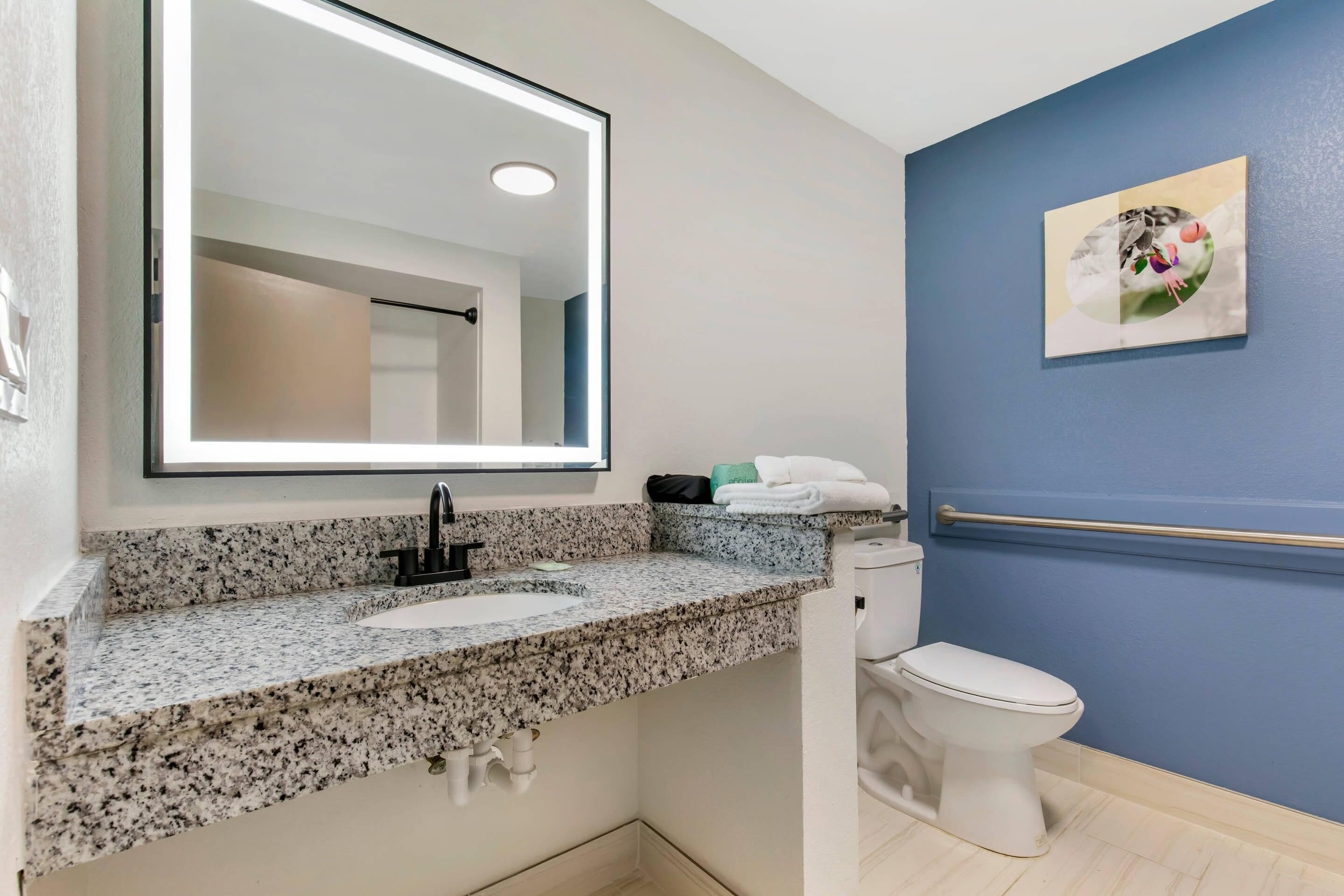 A bathroom with a granite countertop sink, a mirror, a toilet, and a blue wall.