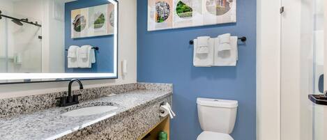 A modern bathroom with a granite countertop sink, a white toilet, and a large mirror.