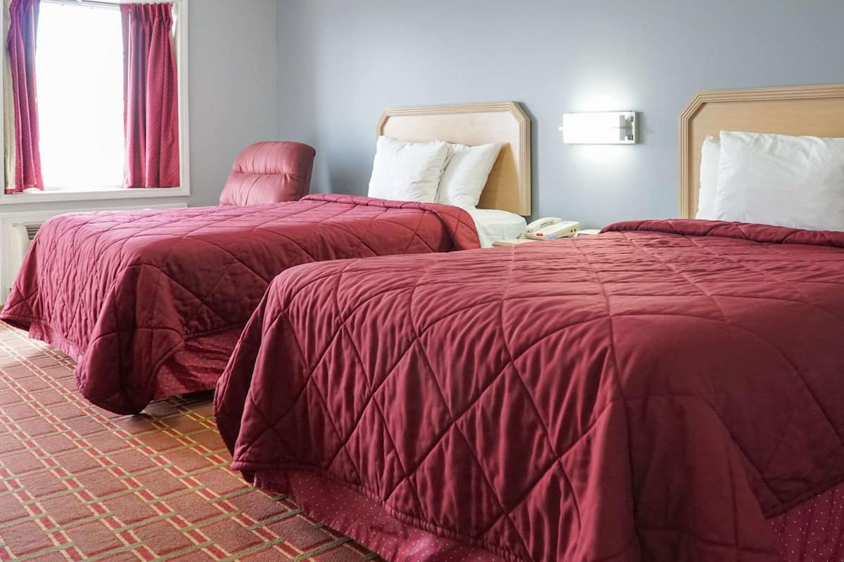 A hotel room with two beds, each with a wooden headboard and white pillows. There is a red chair and a bedside table with a phone.
